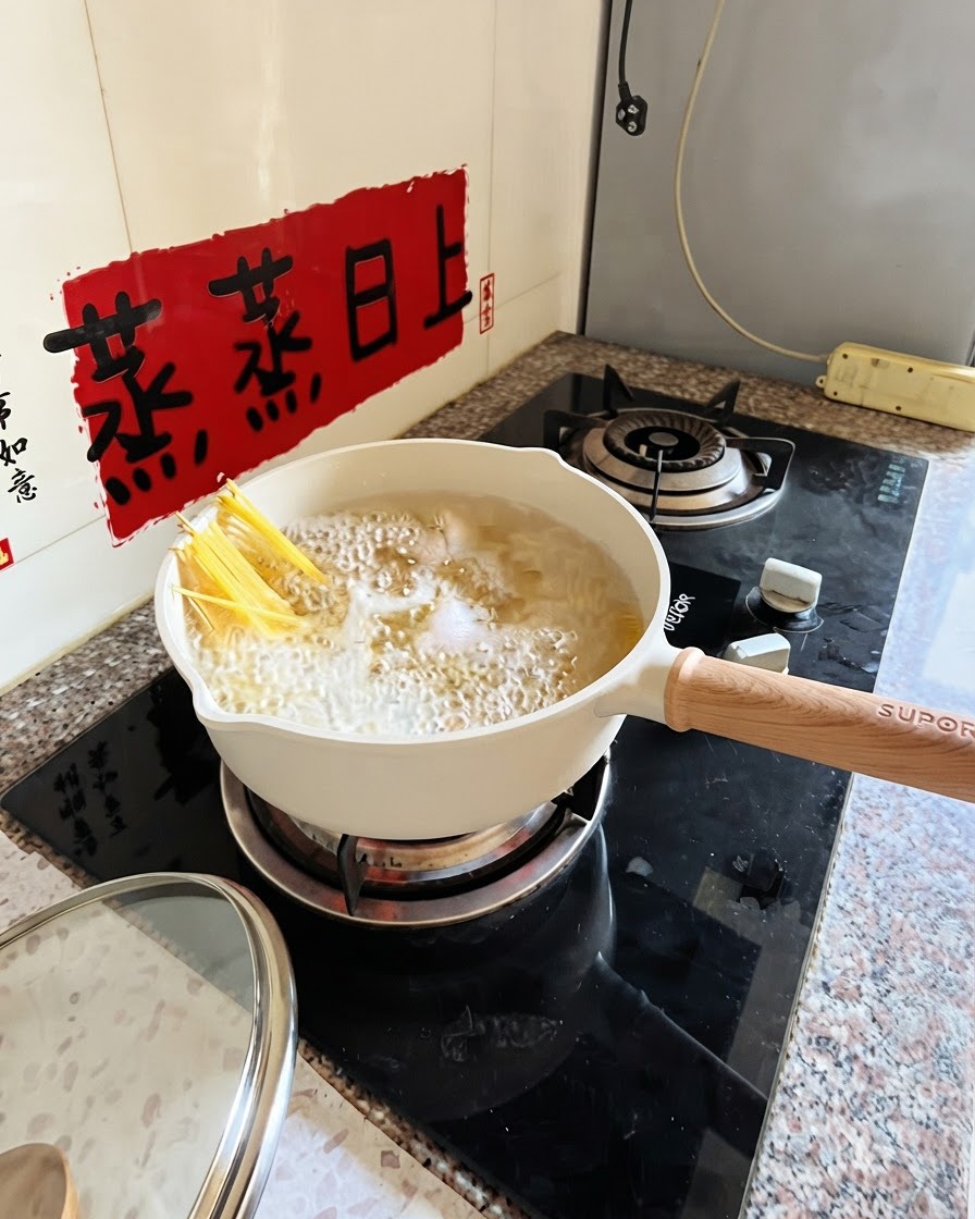 白い鍋で茹でられているスパゲッティを、トングで部分的に沈めている様子