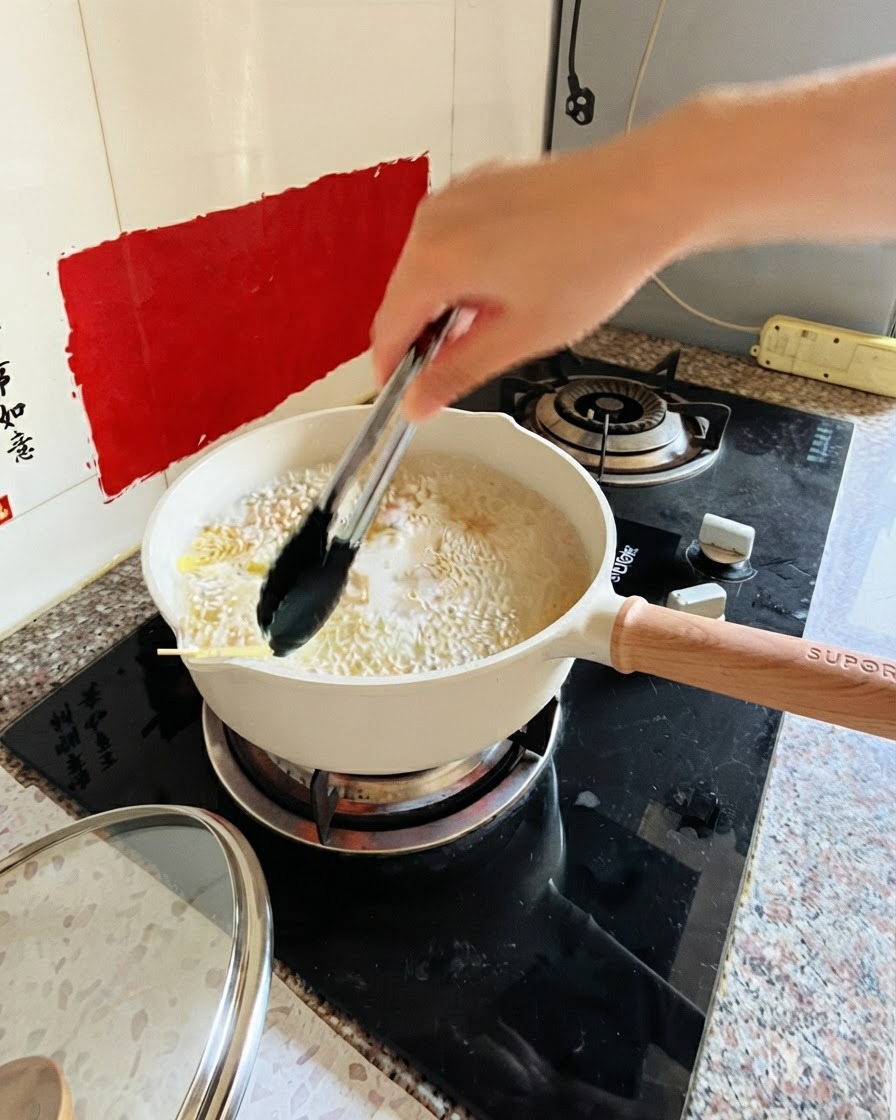 コンロの上の沸騰したお湯とパスタの入った鍋をトングで混ぜている様子