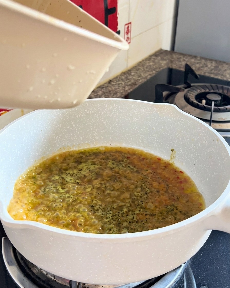 仕上げの和え物の最中に、茹で上がったスパゲッティと液体がフライパンで合わさっている様子