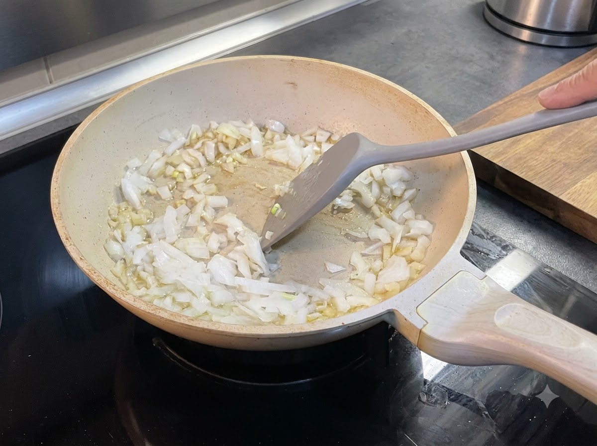 みじん切りにした玉ねぎを、フライパンの中で溶けたバターとヘラで混ぜ合わせている様子。