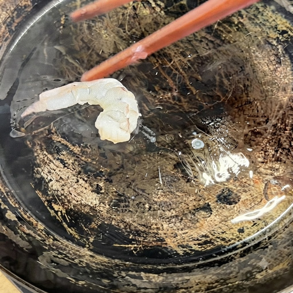 調理用の箸を使って、背開きにした海老が油を引いた熱々のフライパンに入れられている様子。