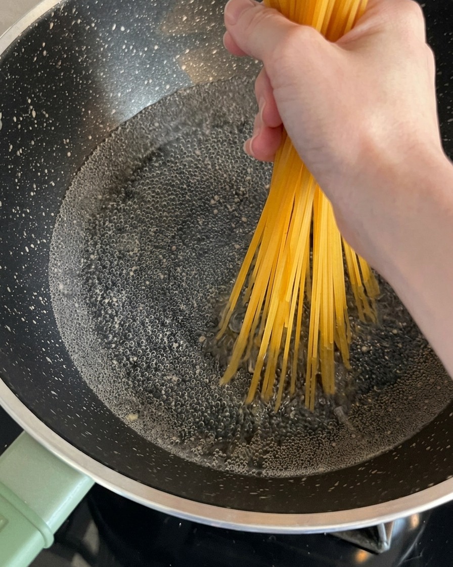 手で持った乾燥スパゲッティを、沸騰したお湯の入った鍋に入れている様子。