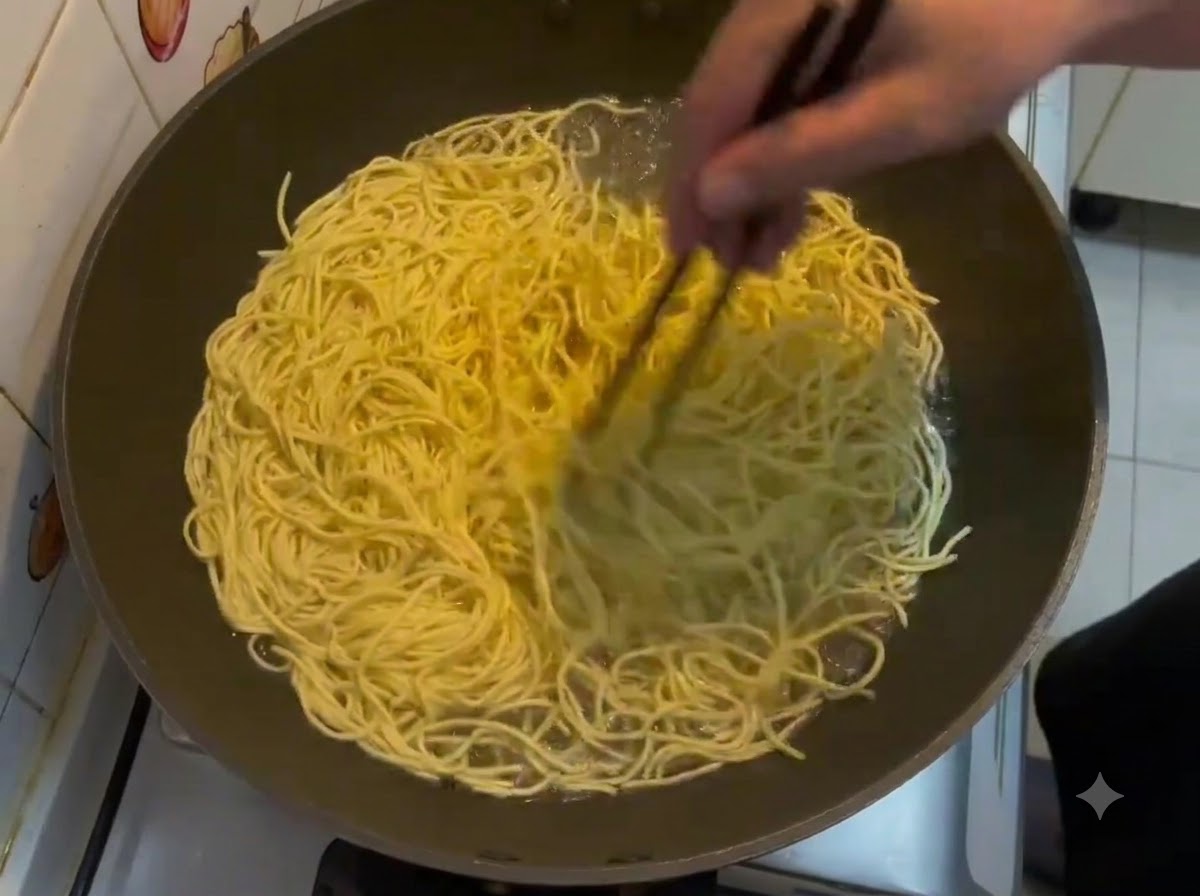 中華鍋の中で沸騰している黄色い伊府麺を、箸でかき混ぜているところ。