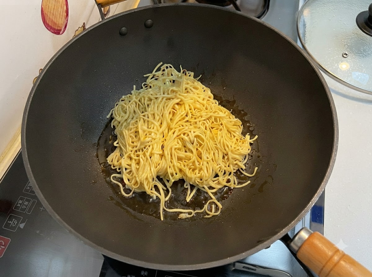 黒い中華鍋の中で、水気を切った伊府麺をスパチュラを使って炒めているところ。