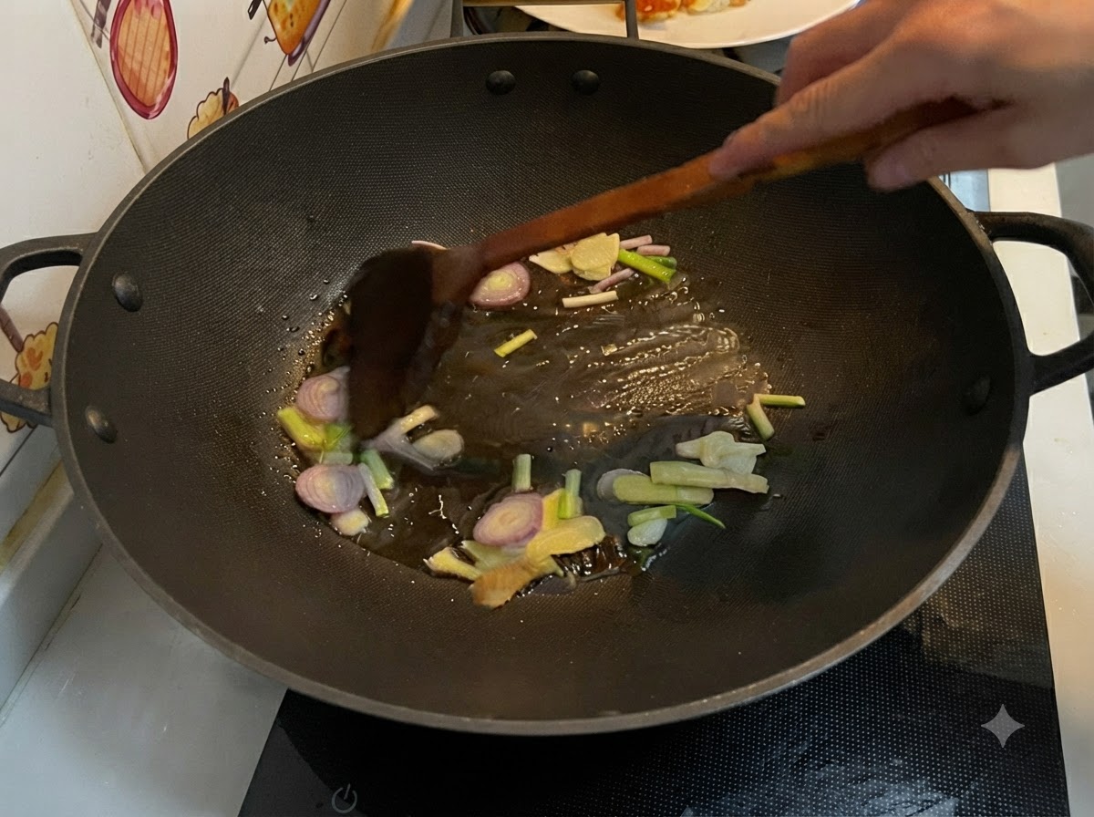 中華鍋の中で熱した油でスライスした生姜、ニンニク、エシャロット、万能ねぎを木べらで炒めているところ。
