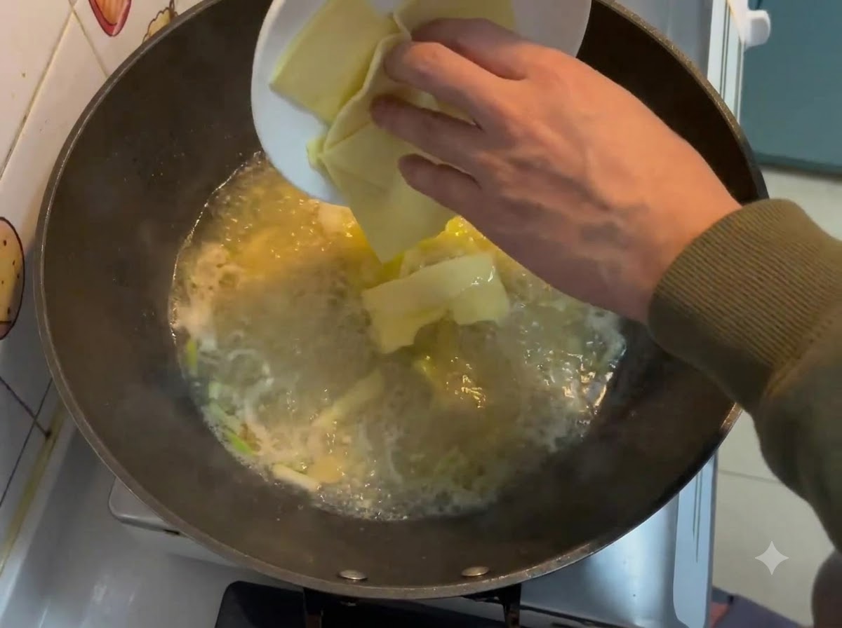 白い皿から四角いチーズのスライスを、中華鍋の中の泡立つクリーミーなスープに落とし込んでいるところ。