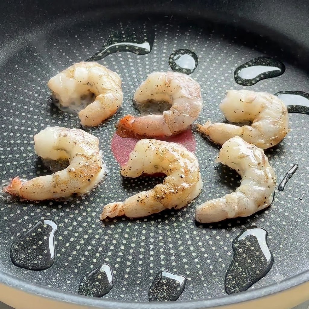 オイルをひいたノンスティックのフライパンで、下味をつけた海老がジューシーに焼けているところ。