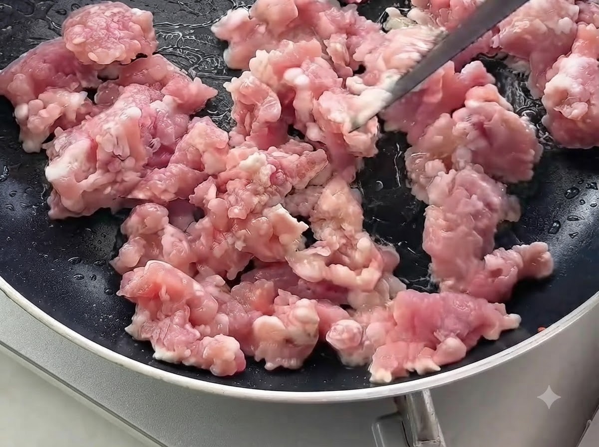 黒いフライパンの中で生の豚ひき肉を炒めている様子。