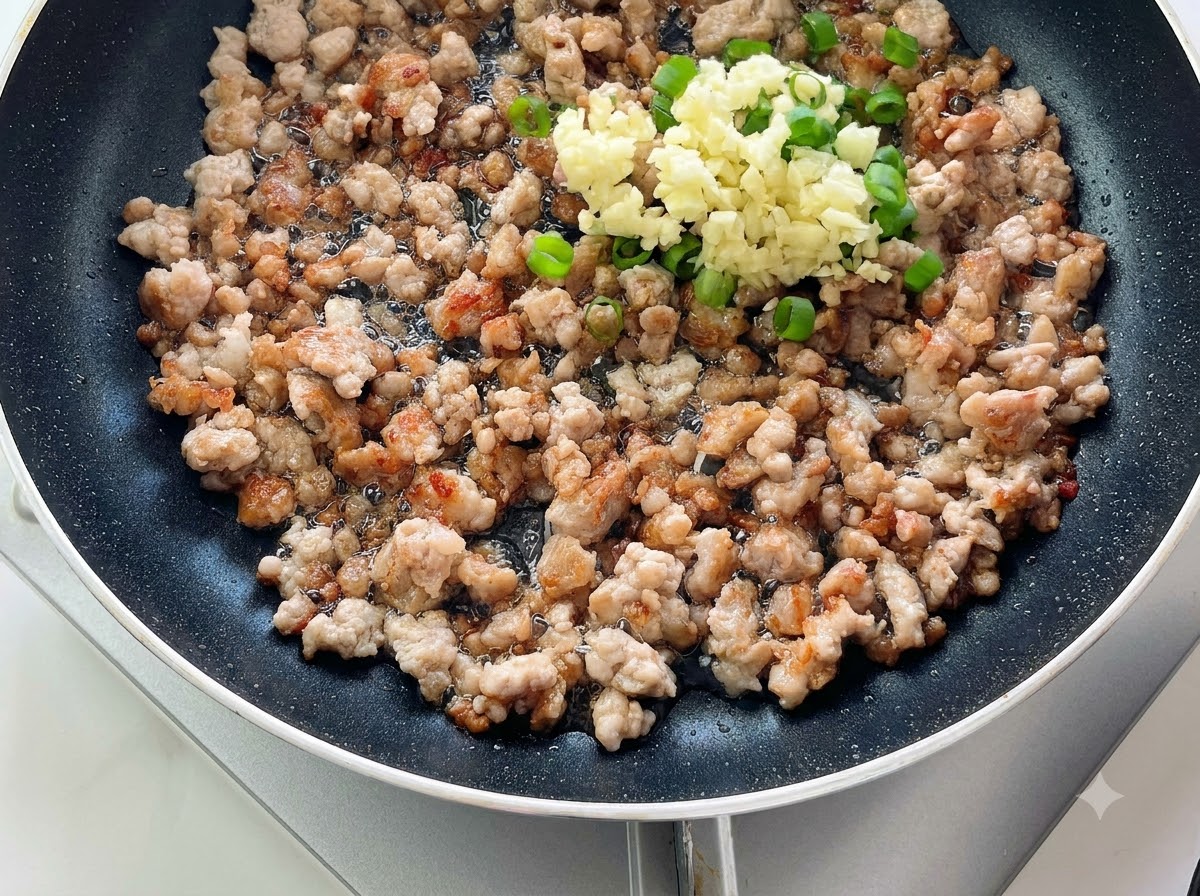 炒めた豚ひき肉の上に、みじん切りにしたにんにくとねぎが乗っているフライパン。