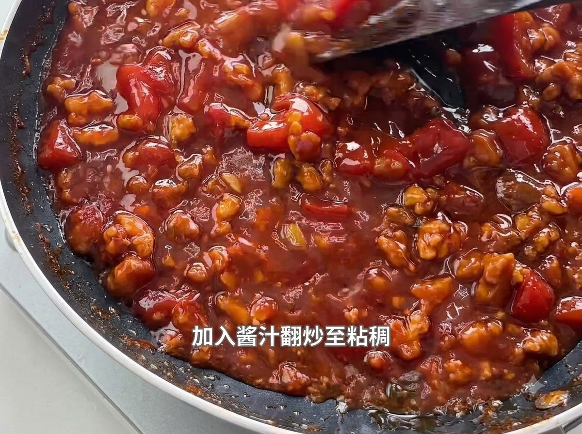 フライパンの中でグツグツと煮立つとろみのあるトマトミートソースをヘラでかき混ぜている様子。