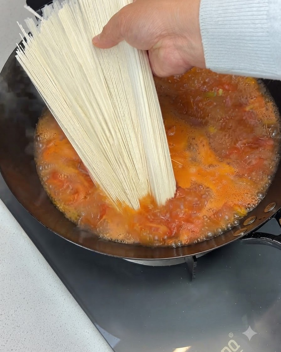 沸騰しているトマトスープが入った中華鍋に、乾燥麺の束を入れようとしているところ