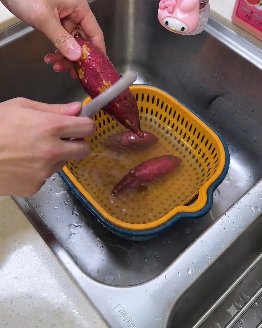 キッチンのシンクでピーラーを使い、生のさつまいもの皮をむいている様子。