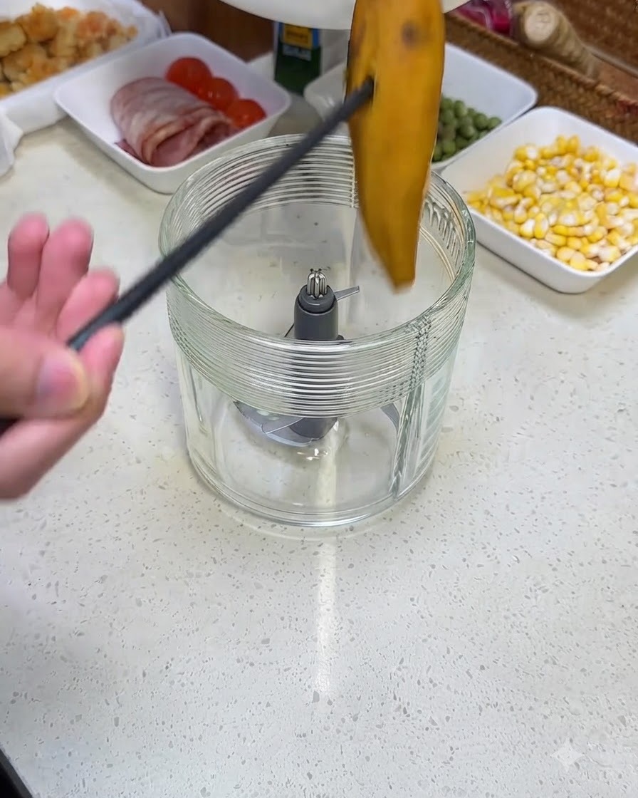 黒いトングを使って、茹でたさつまいもをガラス製のブレンダー容器に入れている様子。