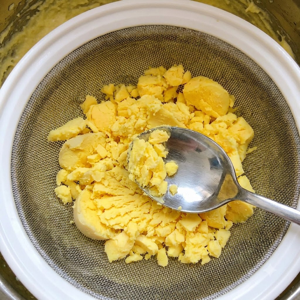 金属製のスプーンを使い、ゆで卵の黄身を網で裏ごししている様子。