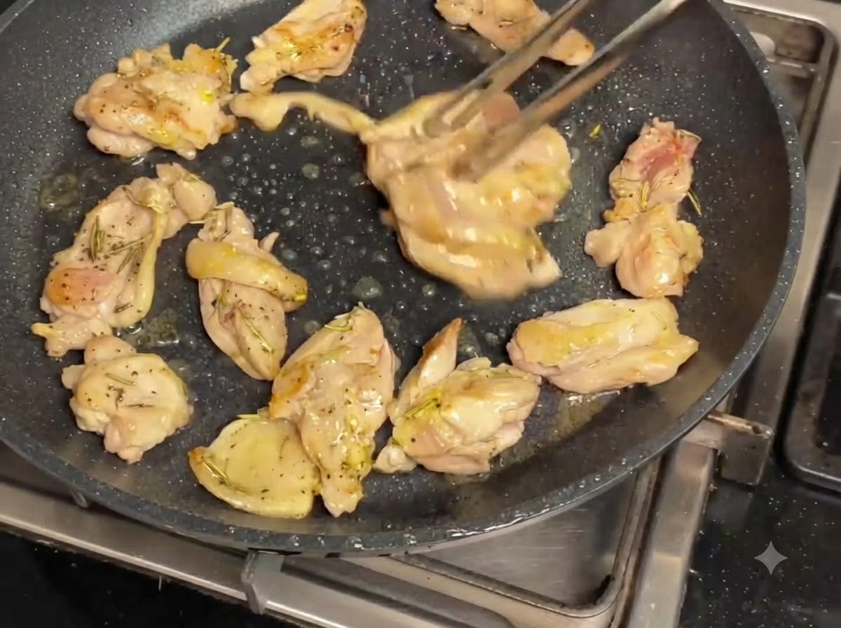 黒いノンスティックフライパンで、鶏肉とマッシュルームがトングで返されながらジューシーに炒められている様子。