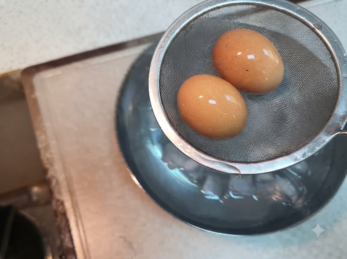 氷水の入ったボウルの上にかざされた、ワイヤーメッシュのストレーナーの中に置かれた2個の茹で卵。