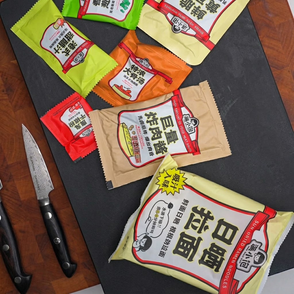 調味料の小袋やソースのパウチ、包丁が暗い色の台の上に並べられている様子。