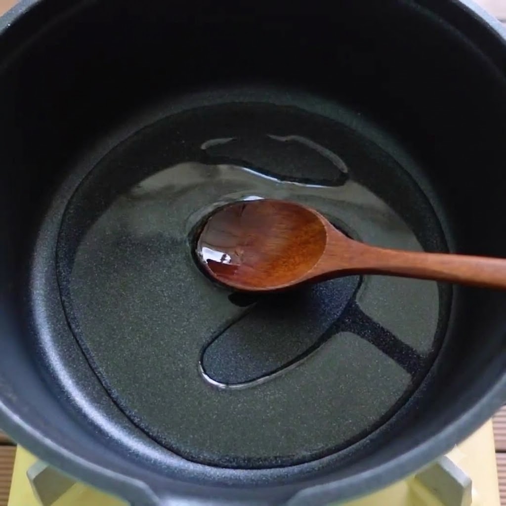 黒い鍋の中で木べらが油と溶けた材料を混ぜ合わせている様子。
