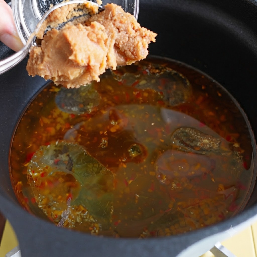 味付けされたスープの入った鍋に味噌を加えている様子。