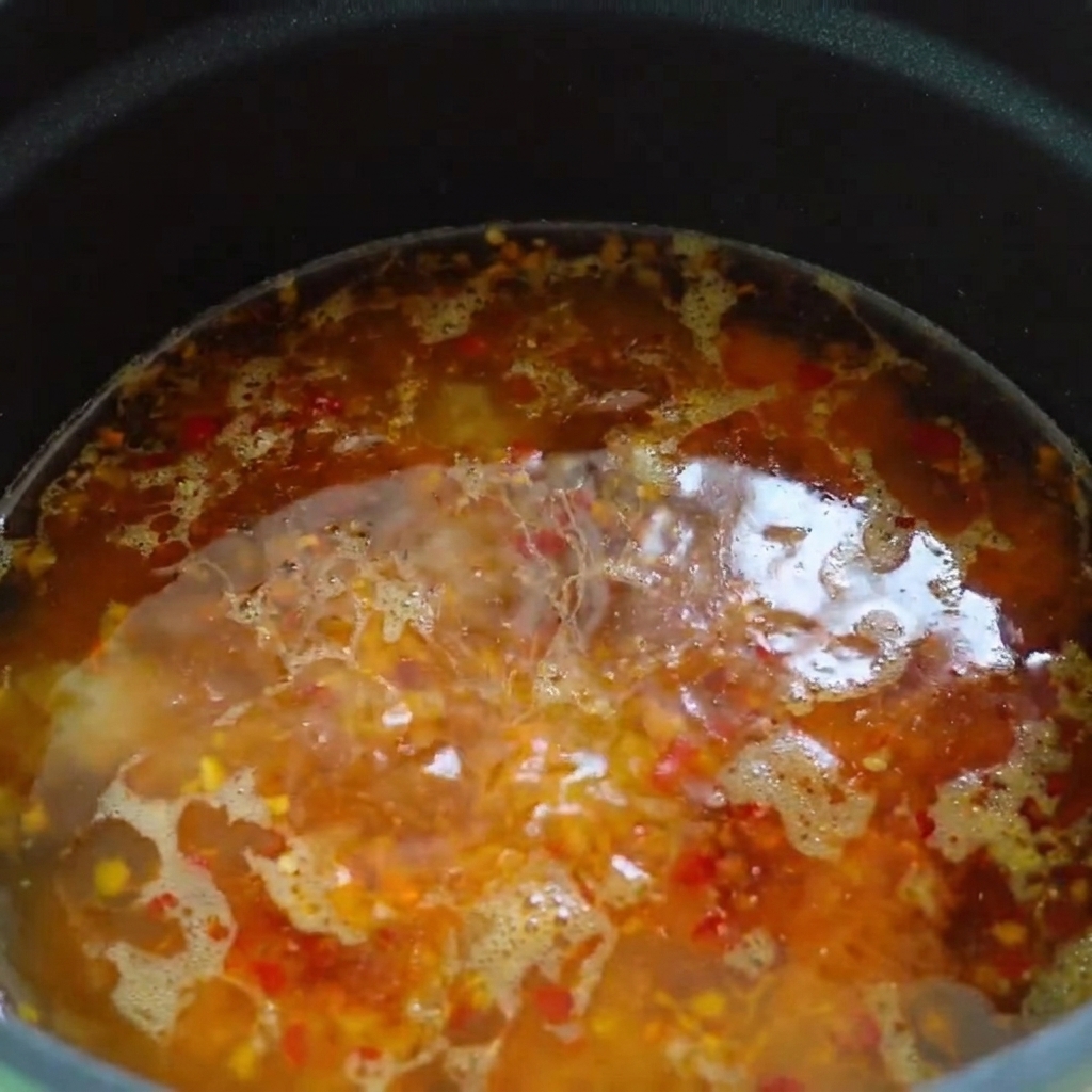 熱いスープベースの表面にラー油とごま油が回しかけられている様子。