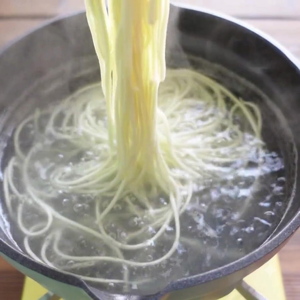 箸で沸騰したお湯から茹で上がったラーメンの麺を引き上げている様子。