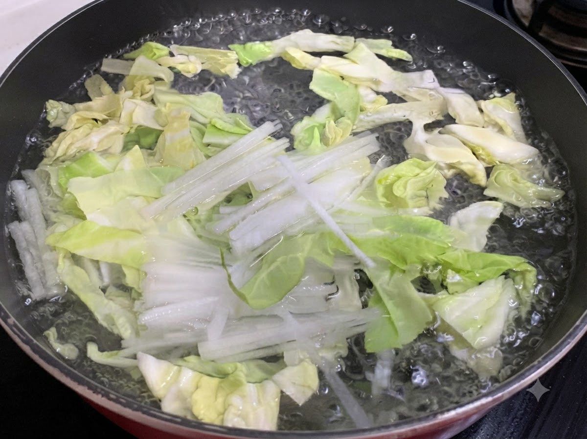 鍋の湯で茹でられている千切りキャベツと大根。