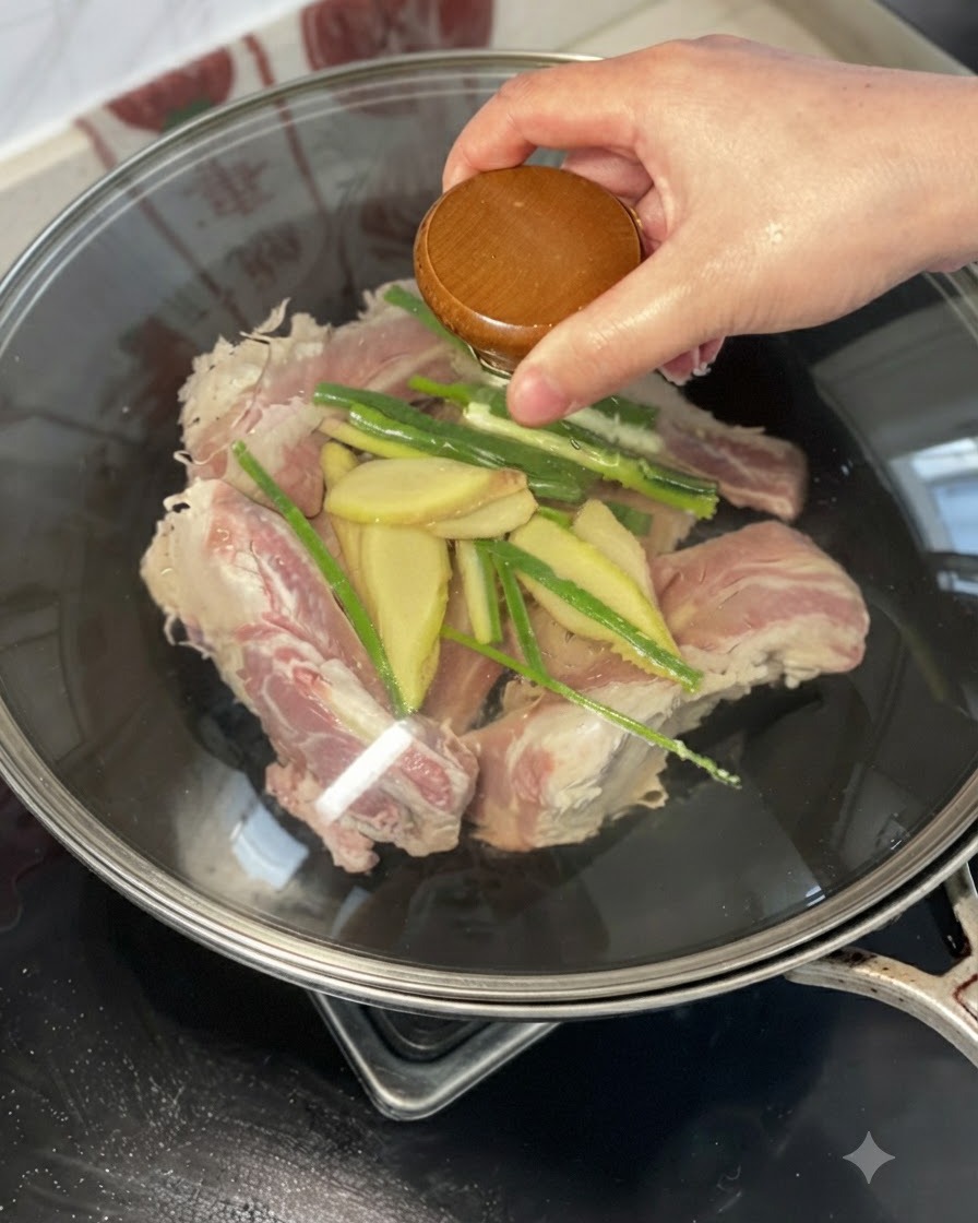 中華鍋の中の牛肋肉、生姜、長ねぎの上から黄酒を回しかける様子