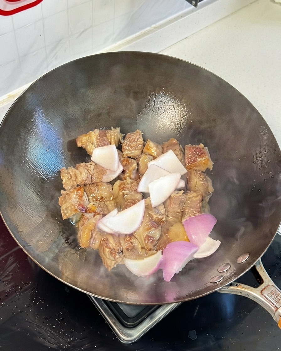中華鍋で炒めた牛肋肉に玉ねぎと各種醤油を加えて混ぜ合わせている様子