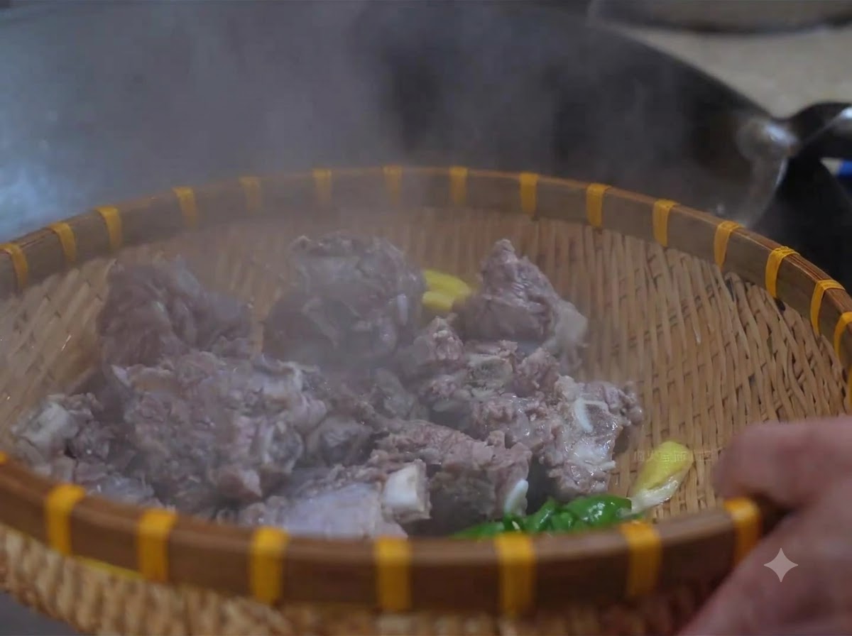竹のザルに入れられた下茹で済みの牛スペアリブを温水で洗っている様子。