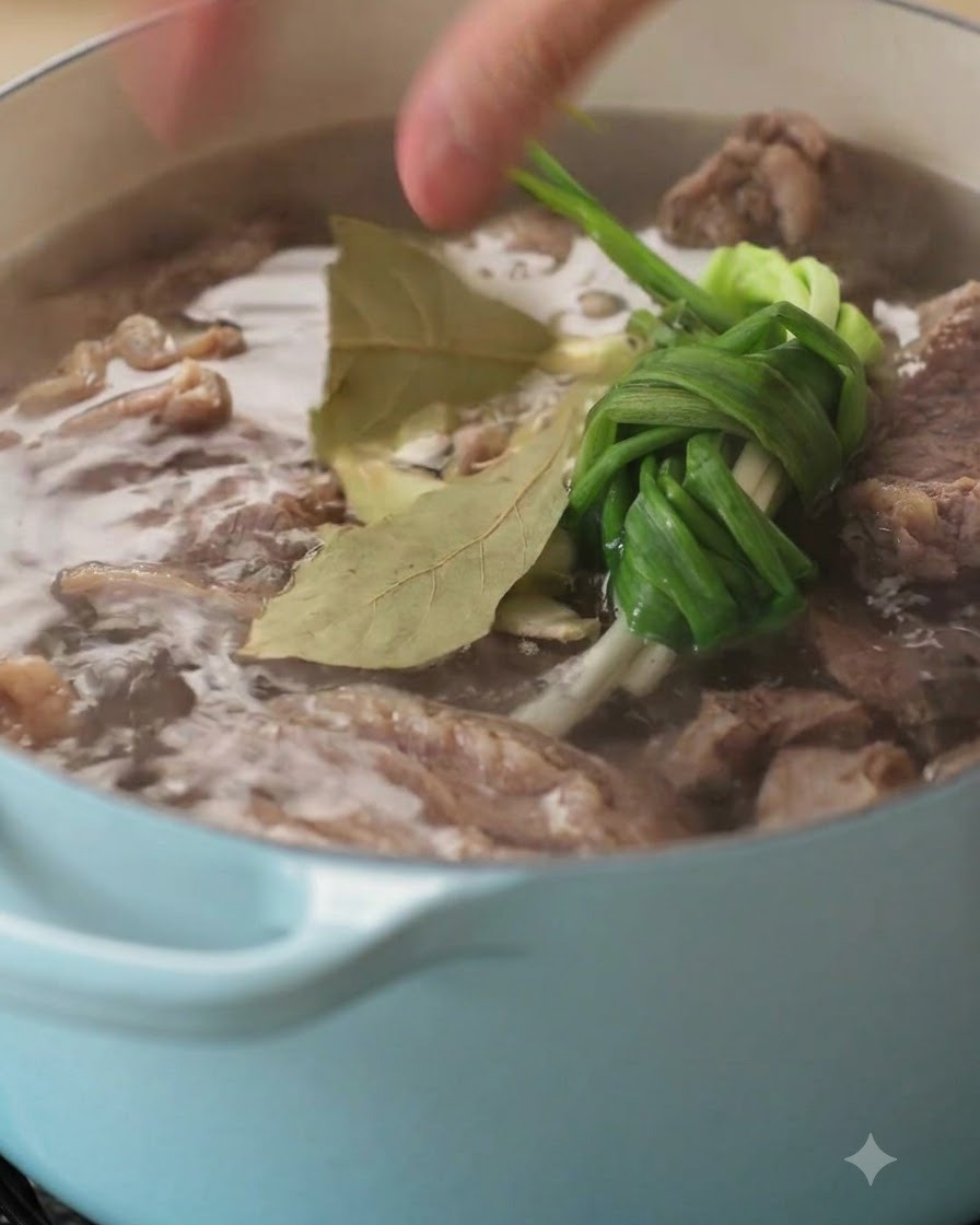 煮込んでいる牛のスープの中に、香辛料と香味野菜が投入される瞬間を捉えたクローズアップ画像。