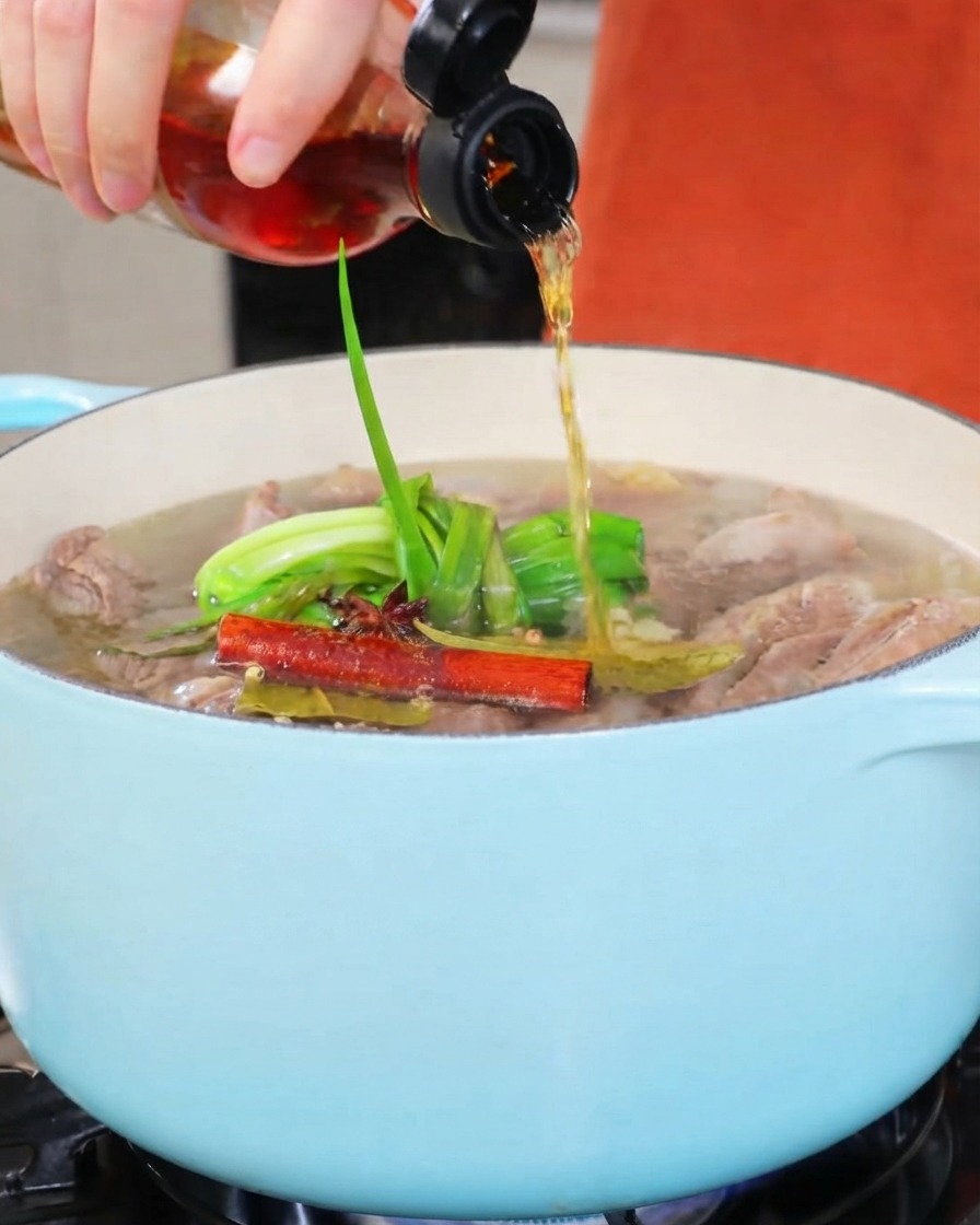 明るい色の煮込み鍋に、小さな瓶から料理酒が注がれている様子。