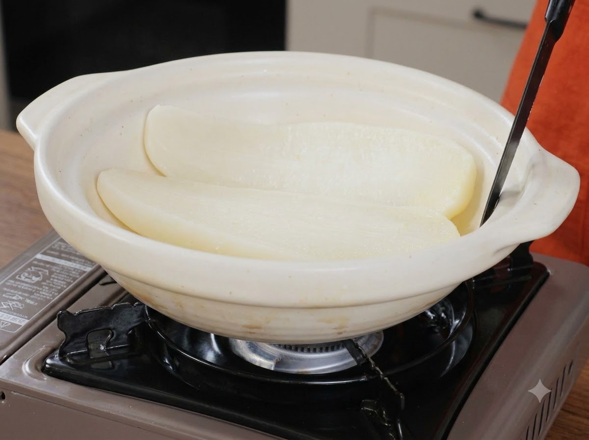 白いセラミック製の広い盛り付け鍋の中に、調理された大根の半月切りが置かれている様子。