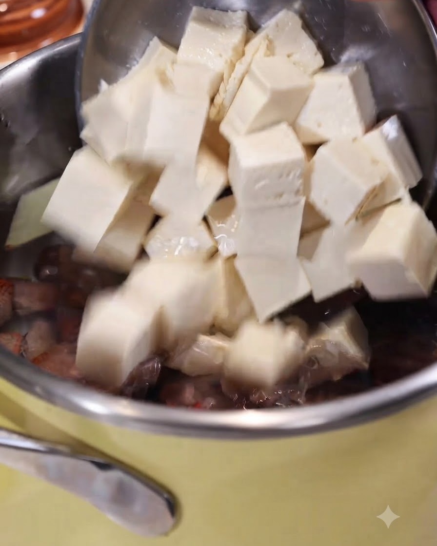 生姜とアサリの入った沸騰したお湯の鍋に、穴あきスプーンを使ってサイコロ状の豆腐を滑り込ませている様子。
