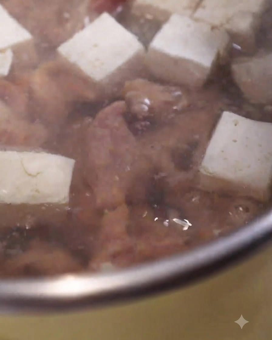白く角切りされた豆腐と一緒に、下味をつけた豚肉のスライスがぐつぐつ煮えるスープの鍋の中で調理されている様子。