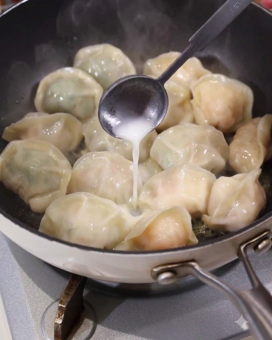 熱いフライパンの中の餃子の隙間に、スプーンを使って白い液体状のバッター液を均等に注ぎ入れている様子。