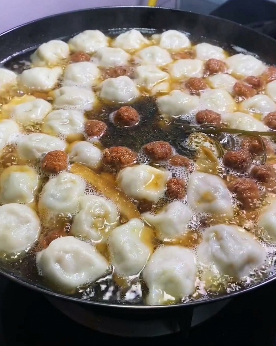 大きな鍋で煮込まれる餃子や具材にダークソイソースが加えられ、深い色合いを与えているところ。