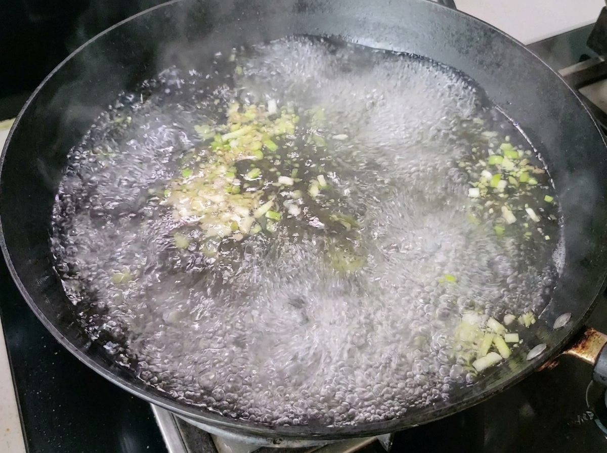 ネギと生姜を入れた沸騰したお湯から湯気が出ている中華鍋。