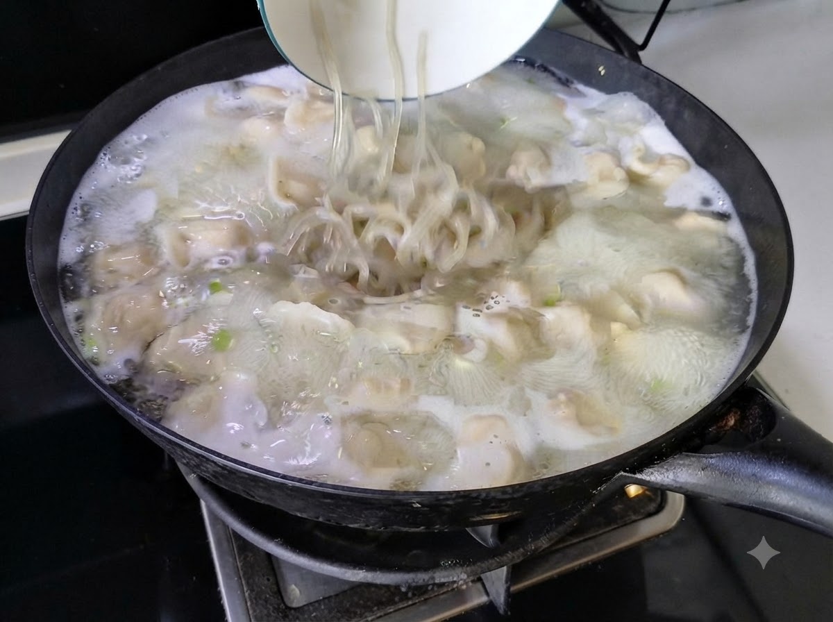 白いボウルから、中華鍋で煮立っている餃子スープの中に麺が投入されている様子。