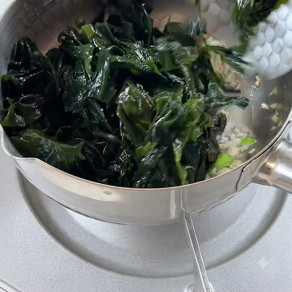 炒めたニンニクとネギが入った鍋に、水切りした戻し海草が加えられている様子。