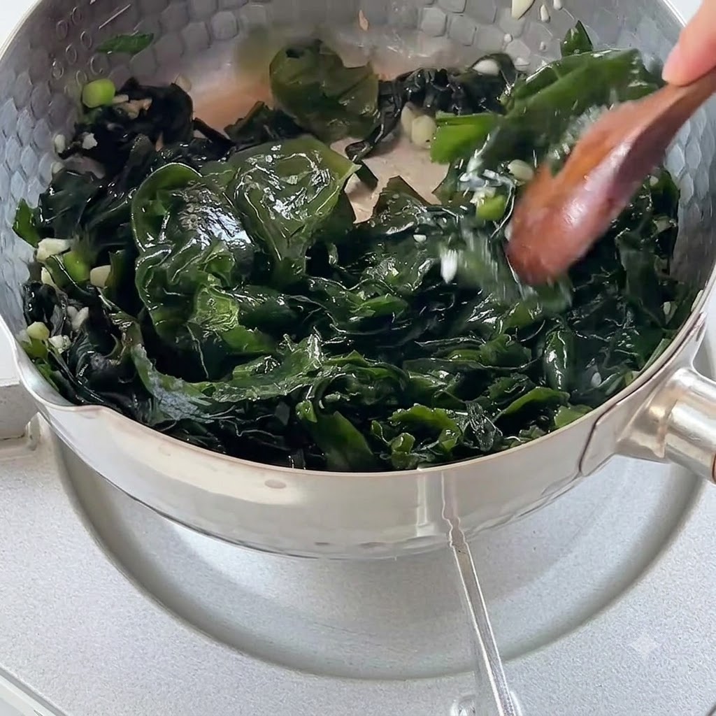 炒めた海草と香味野菜が入った鍋に、熱湯が注ぎ込まれている様子。
