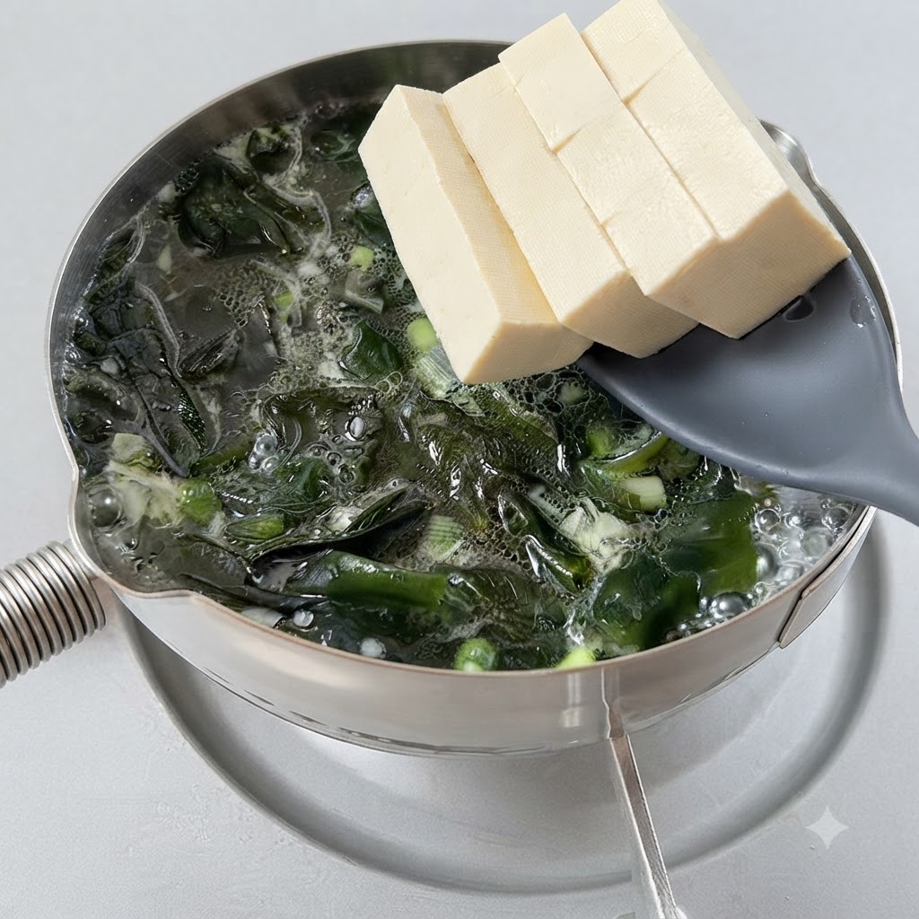 穴あきスプーンを使って、煮立っている海草スープの中に豆腐の角切りが移されている様子。