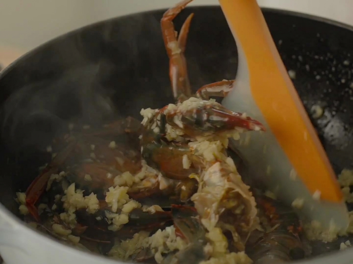 蒸気の上がる鍋の中で、シリコンスパチュラを使ってカニとエビを混ぜ合わせているところ。