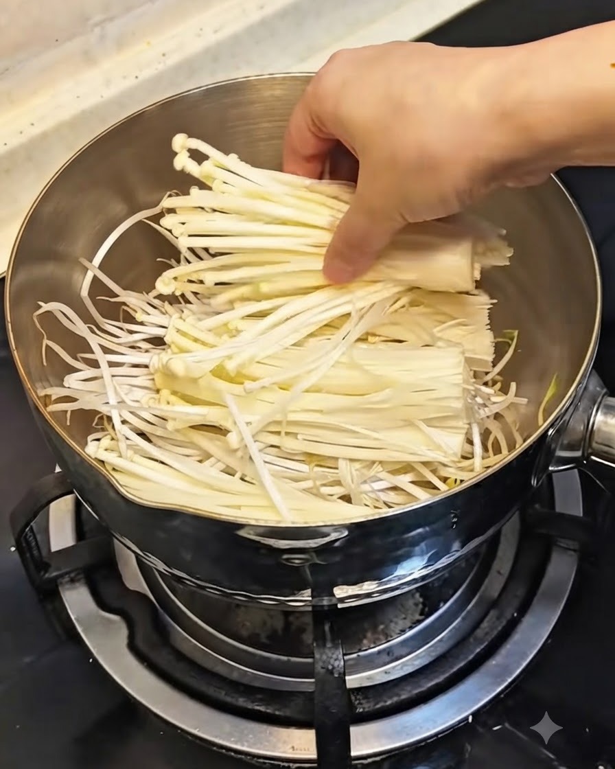 鍋のもやしの上に、新鮮な白いえのき茸をのせる様子。