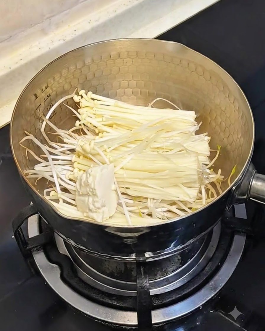 もやしとえのき茸が入った鍋に、柔らかい絹ごし豆腐をスプーンですくい入れる様子。