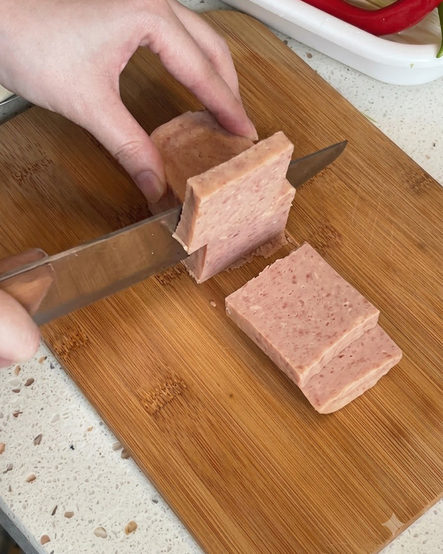 まな板の上で、缶詰のランチョンミートのブロックを厚切りにしている様子。