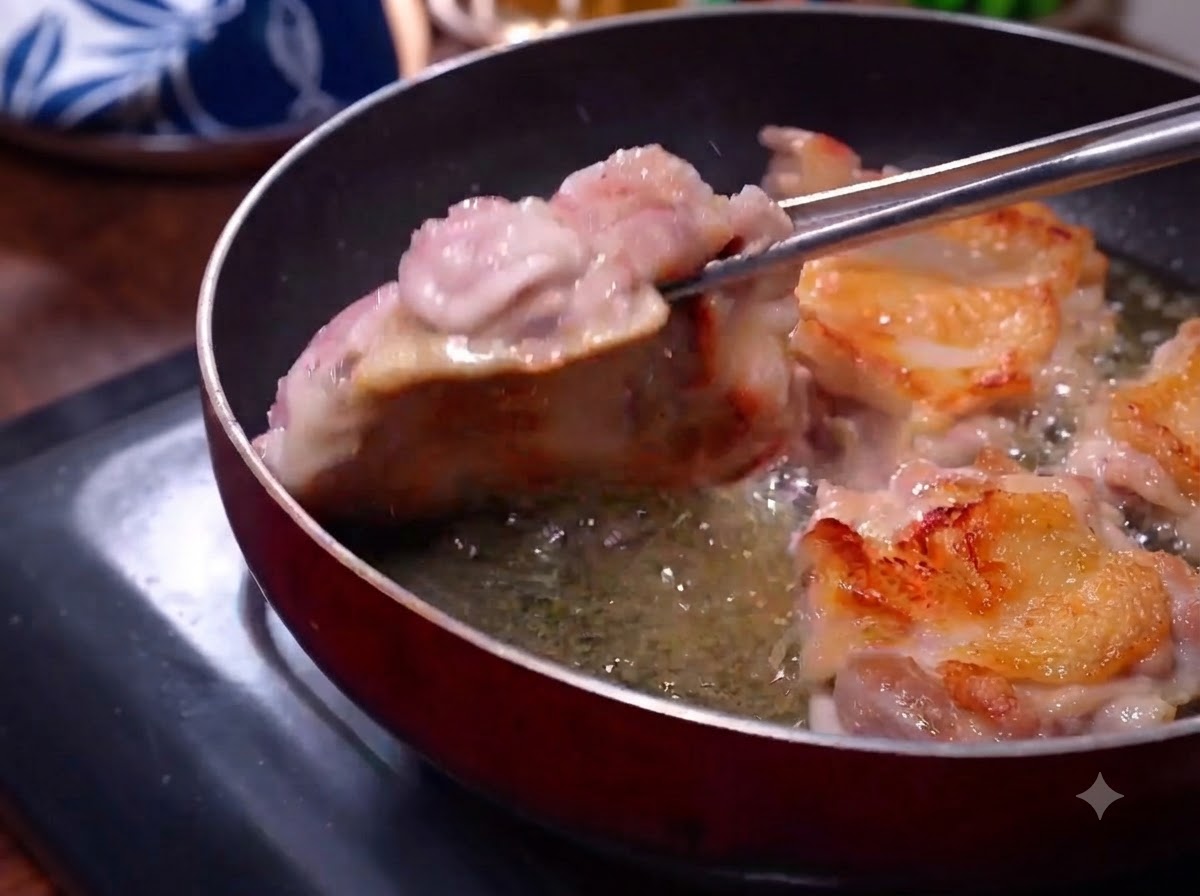 フライパンでこんがりと焼き色のついた鶏肉をトングで裏返している様子