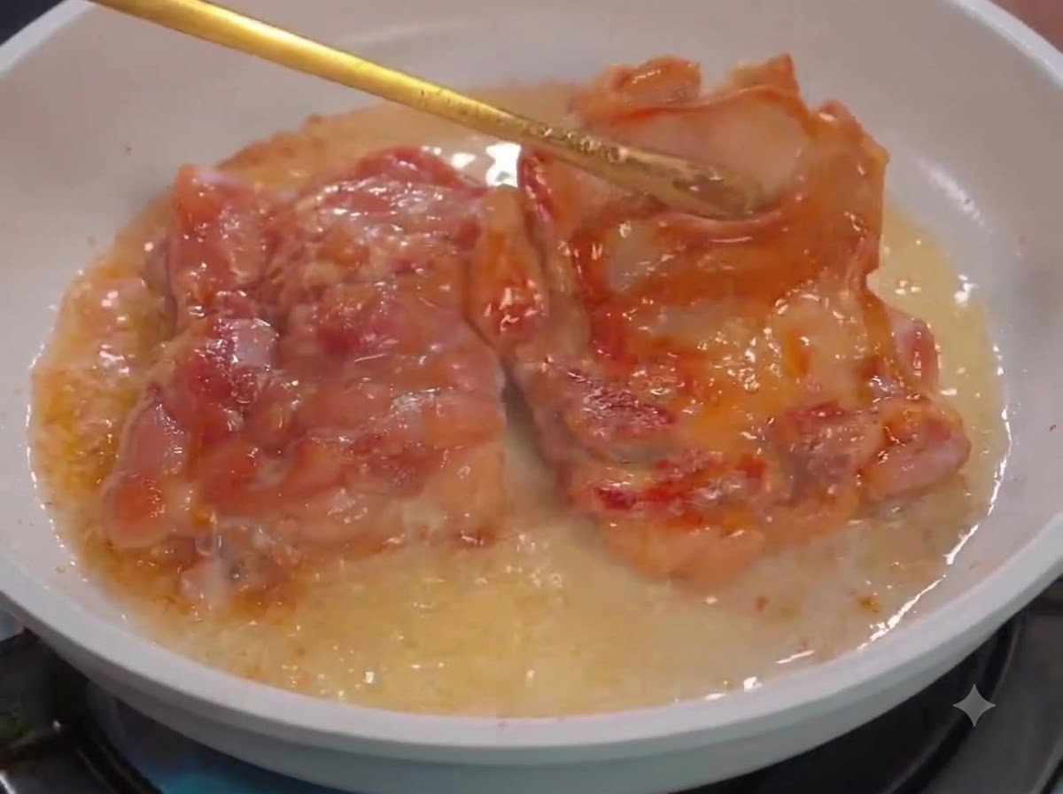 白いフライパンの中でキッチンングトングを使い、油を引いて鶏肉を裏返している様子。