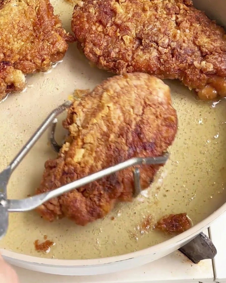 油の入ったフライパンから、ステンレス製のトングを使ってカリッと揚がったチキンチャップを持ち上げている様子。