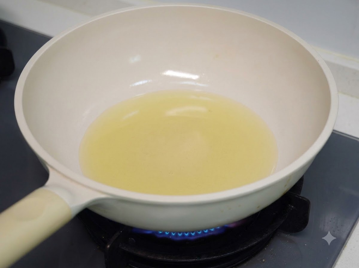 ガスコンロの上の白いフライパンで調理用油を加熱している様子。