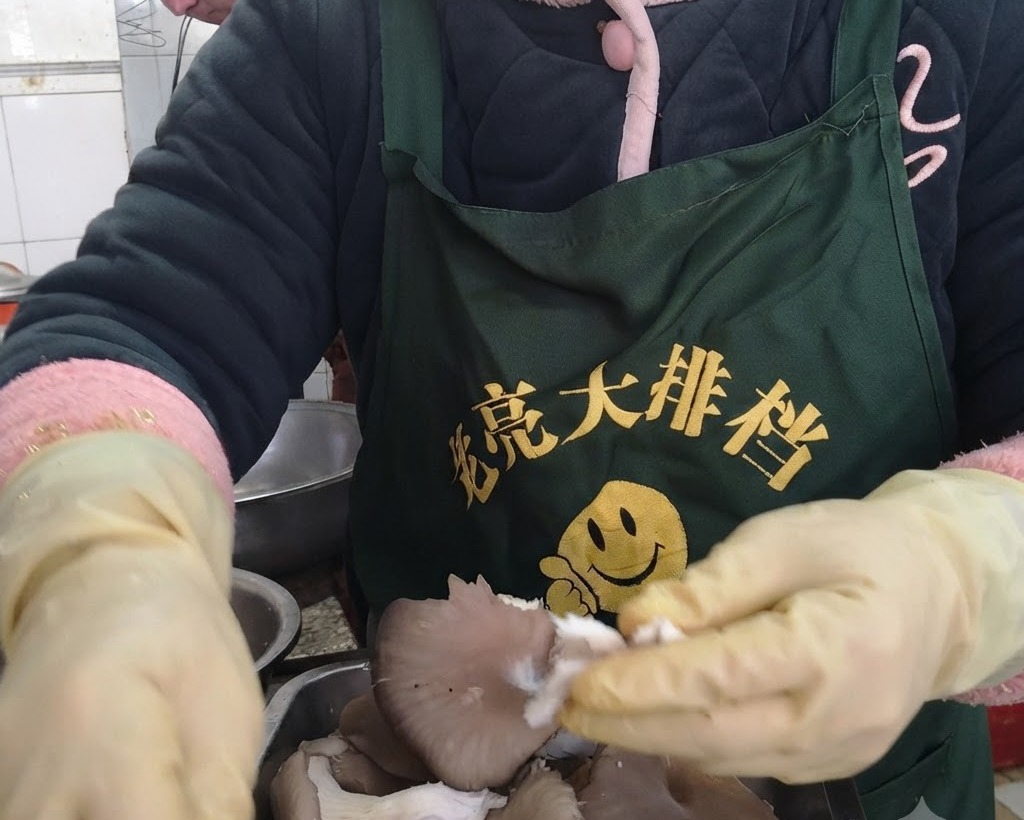 保護用手袋を着用した手で、新鮮なひらたけを一口大の細長い房状に裂いている様子。